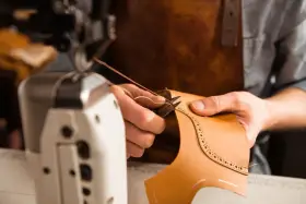 Mani esperte che cuciono la pelle con filo e ago, creando un dettaglio decorativo su un pezzo di cuoio.