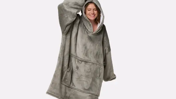 Donna sorridente indossa una felpa oversize grigia, morbida e confortevole, perfetta per chi cerca come ammorbidire tessuti rigidi e godersi il relax.
