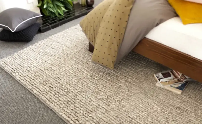 Un grande tappeto di lana intrecciata accanto a un letto. Scopri come lavare un tappeto di lana grande per mantenerlo come nuovo.