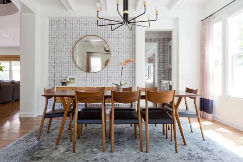 Tavolo da pranzo in legno con sedie in pelle nera, tappeto sotto il tavolo da pranzo si, con carta da parati a motivi geometrici e specchio rotondo.