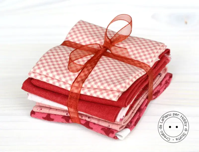 Fazzoletti di stoffa rossi e rosa, con fantasie a quadretti e cuoricini, legati da un nastro. Perfetti per un progetto di cucito creativo.